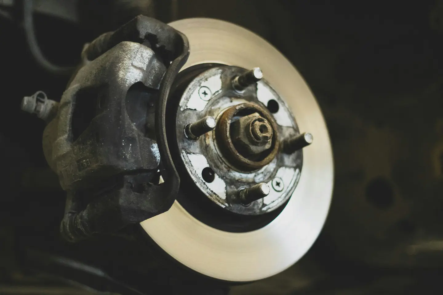 A worn brake caliper and rotor on a car with the wheel off, rust on the hub and the wheel studs.