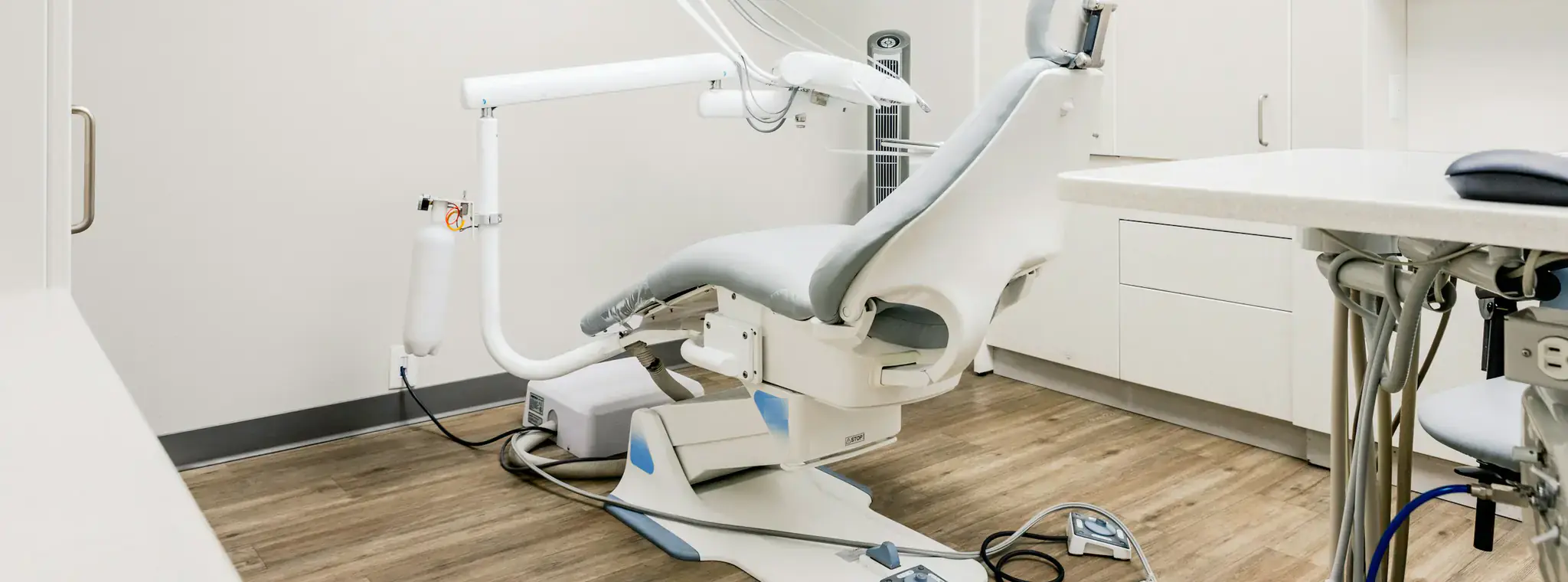 A bright, empty dental treatment room with a grey chair and a wood-look floor.
