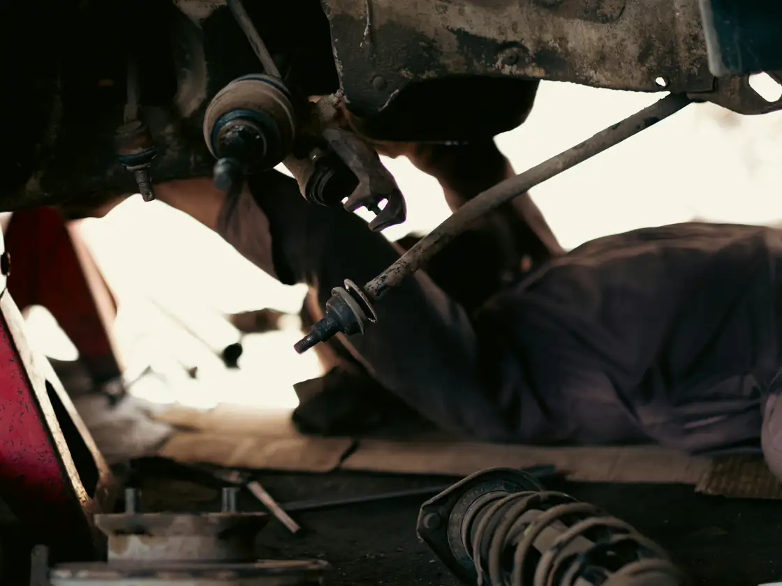 A mechanic working under a car beside a red jack stand.