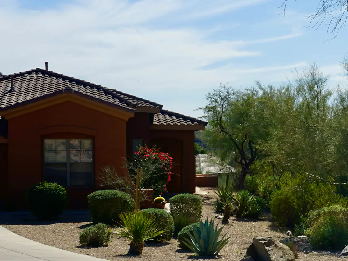 A single-storey tile-roofed house behind a gravel front yard planted with agave, sotol, clipped shrubs and palo verde trees.